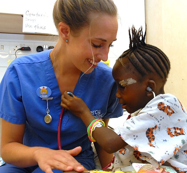 a woman in scrubs is talking to a child with a stethoscope