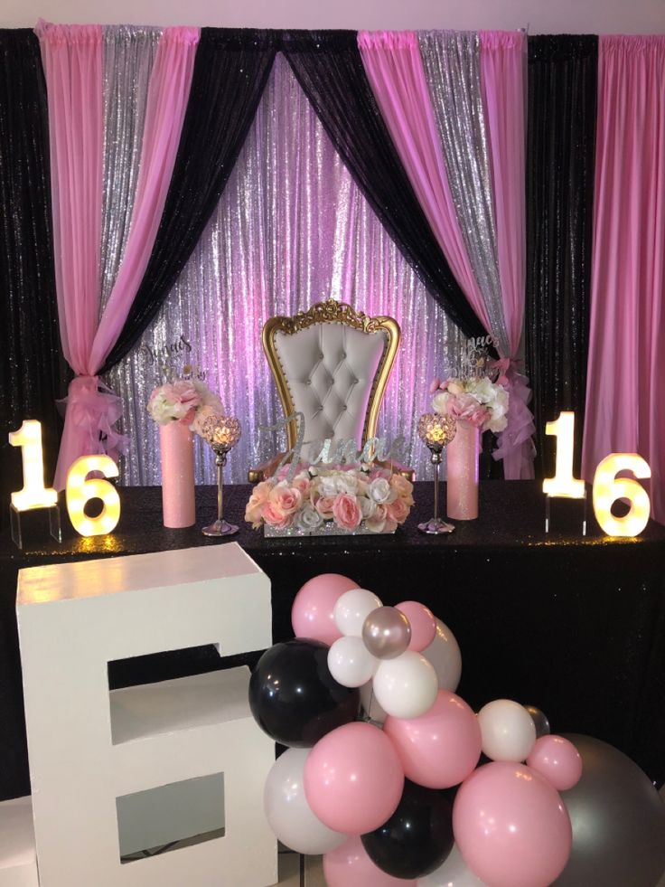 a chair and table with balloons on it in front of a stage set up for a party