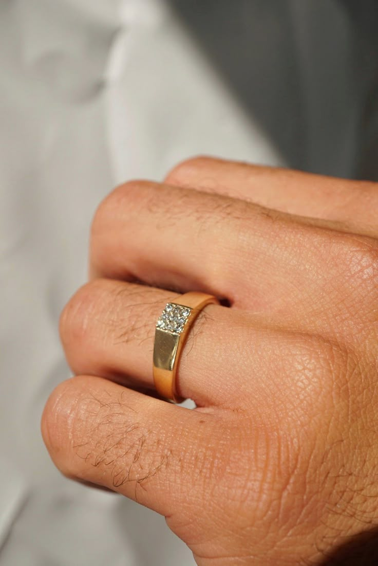 a man's hand wearing a gold ring with two diamonds on the middle finger