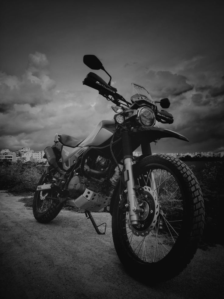 a black and white photo of a motorcycle parked on the side of a dirt road