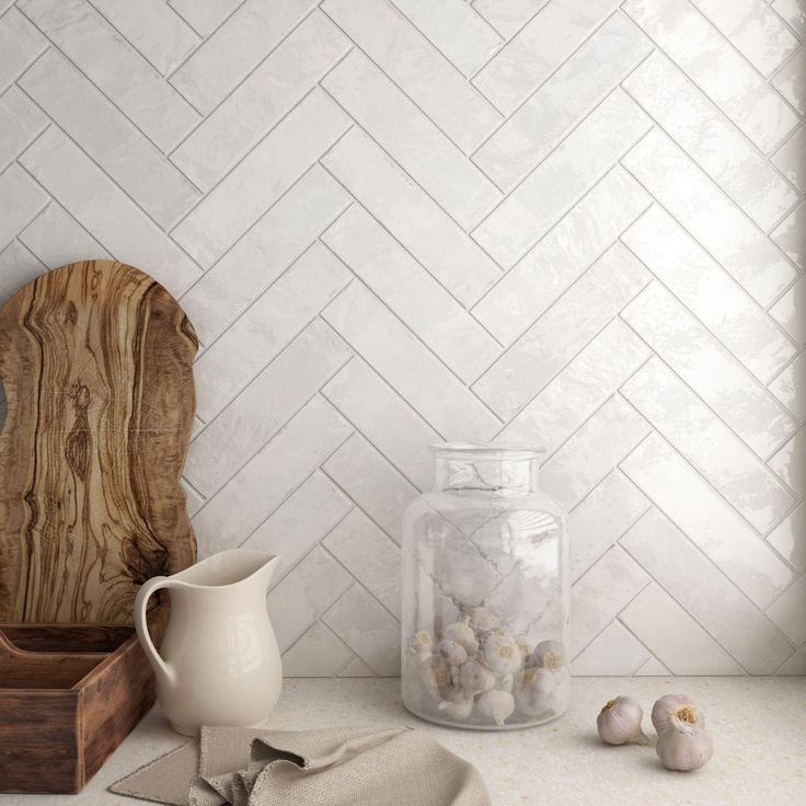 a kitchen counter with white herringbone tile and wooden cutting board, garlic cloves, salt and pepper shaker