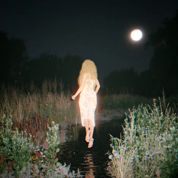 a naked woman is walking in the water at night with her back turned to the camera