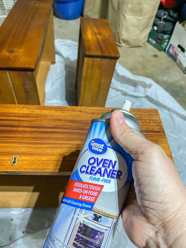 a person is holding a spray bottle in front of a wooden bench and table with other furniture