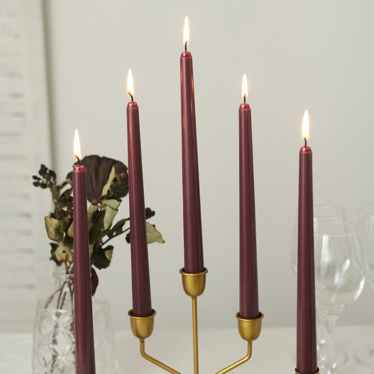 a candle holder with five candles in it on a table next to some wine glasses