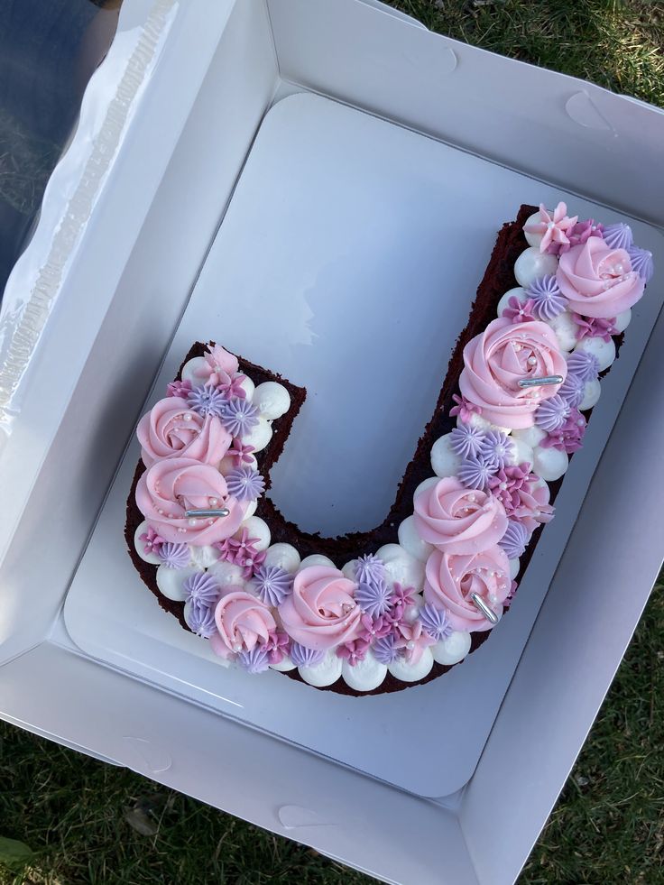 the letter u is decorated with pink and purple flowers on top of chocolate cake in a box