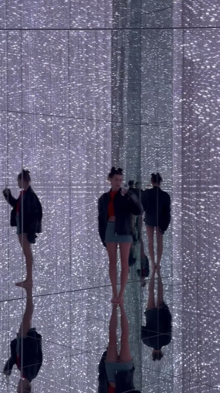 two women in short skirts are reflected in a mirrored wall with silver sequins