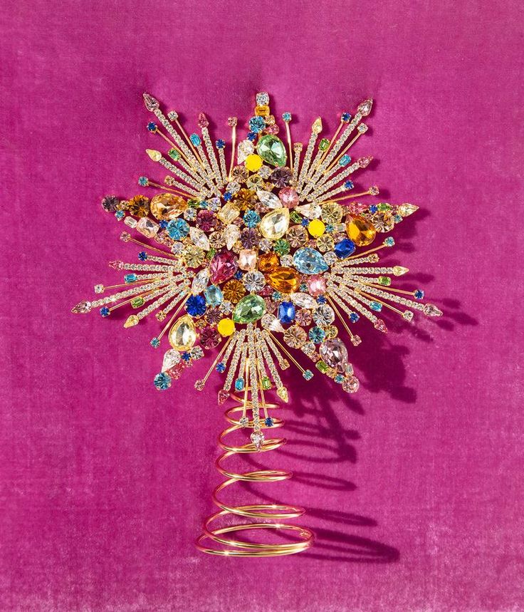 a star shaped brooch with multicolored stones and gold spirals on a pink background