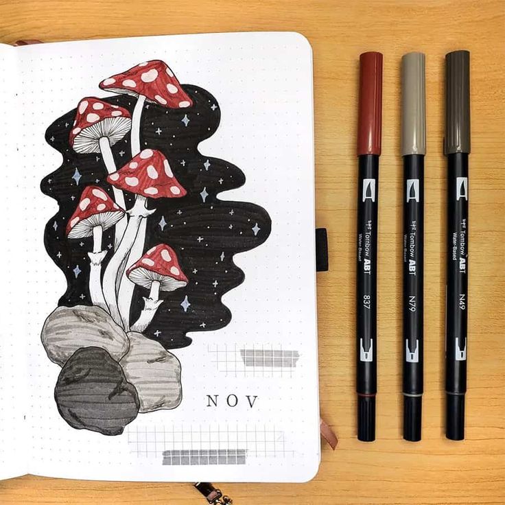 a notebook with three markers and two pens on it next to an open drawing book