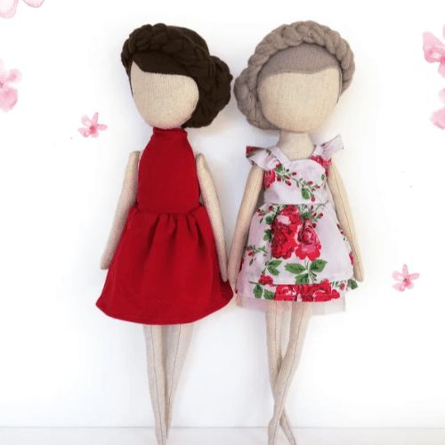 two dolls standing next to each other in front of pink flowers on a white wall