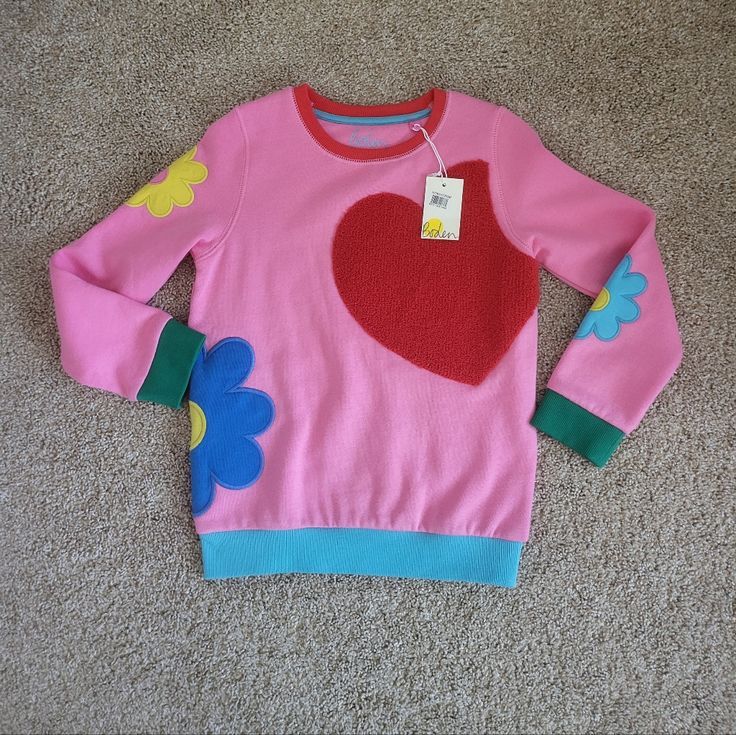 Heavy Pink Sweatshirt Has Multi-Colored Bands, Red Neck, Green Cuffs, And A Blue Banded Waist. The Front Has An Oversized Heavy Red Heart Applique, With Heavy Mod Flower Appliques On Both Sleeves And The Left Side That Wraps Around To The Back. Made Of A Soft Cotton Blend. Size 7/8 Would Look Awesome Paired With Her Favorite Jeans Or Skirt Nwt Never Worn Excellant Condition No Damage Boden Pink Cotton Patchwork Sweatshirt, Playful Winter Sweatshirt For Playwear, Cute Long Sleeve Sweater For Playwear, Playful Long Sleeve Sweatshirt For Playwear, Playful Long Sleeve Playwear Sweatshirt, Pink Patchwork Cotton Sweater, Pink Fall Playwear Top, Cute Long Sleeve Patchwork Tops, Cute Long Sleeve Tops With Patchwork