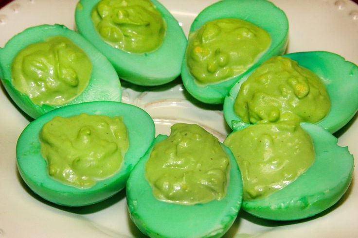 green deviled eggs on a white plate topped with guacamole