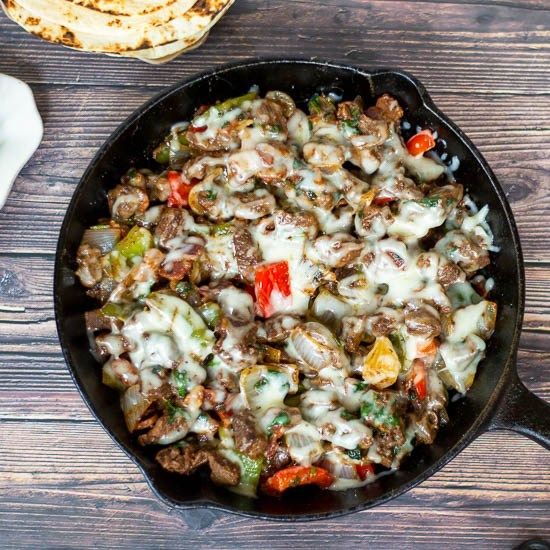 a skillet filled with meat and vegetables on top of a wooden table next to pita bread