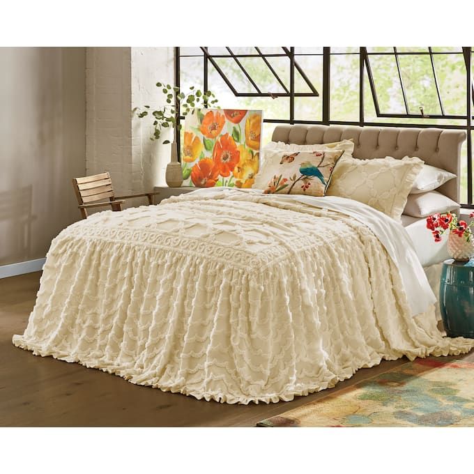 a bed with white ruffled bedspread, pillows and blankets on top of it