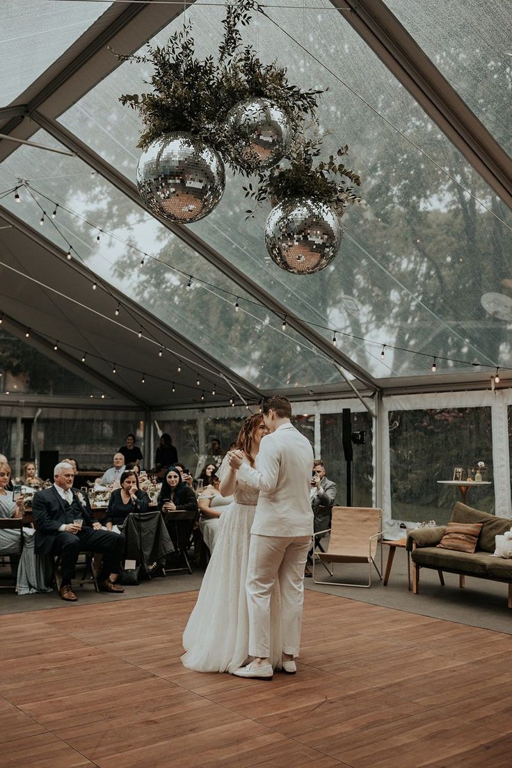 a bride and groom share their first dance under the tented area with hanging decorations