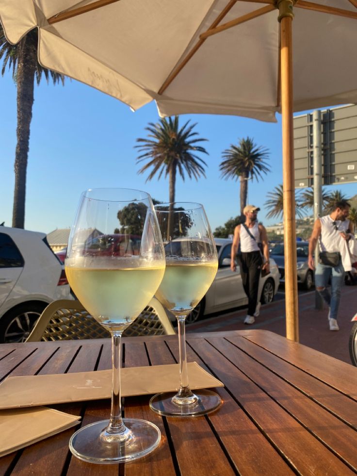 two glasses of white wine sitting on top of a wooden table next to each other