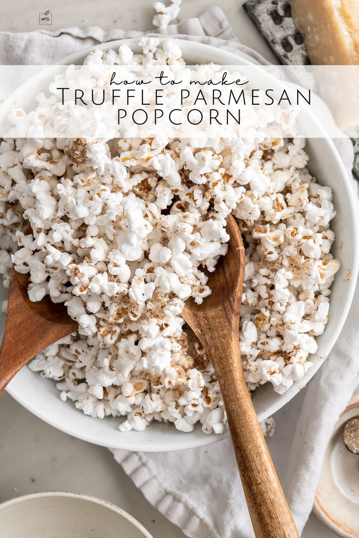 a white bowl filled with popcorn on top of a table next to two wooden spoons