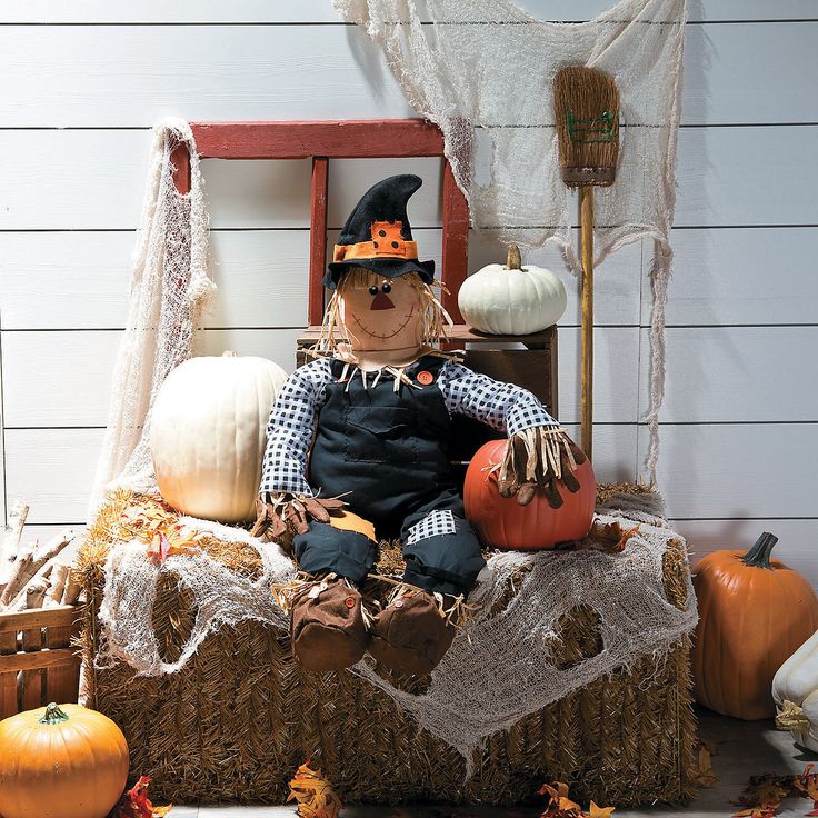 a scarecrow sitting on top of a hay bale filled with pumpkins and other decorations