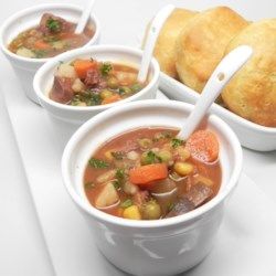 three bowls filled with soup on top of a white plate next to rolls and bread