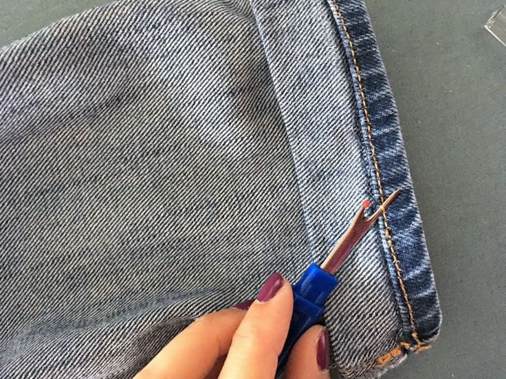 a woman's hand holding a pair of scissors in front of her jeans pocket