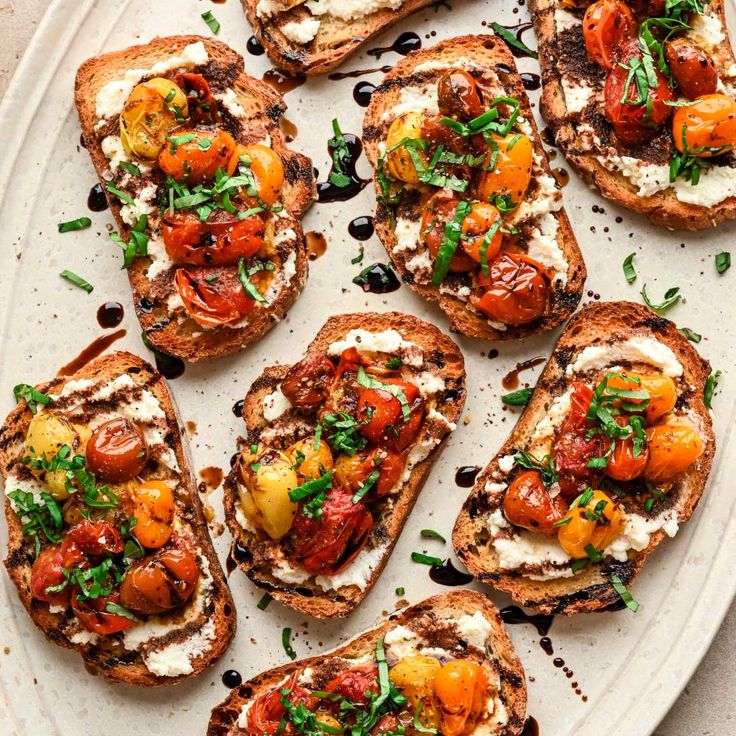 several pieces of bread with tomatoes, cheese and herbs on it sitting on a plate