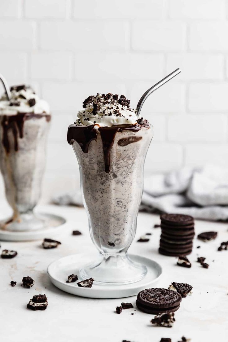 two ice cream sundaes with oreo cookies on the side and white brick wall behind them