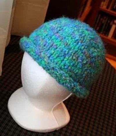 a white mannequin head wearing a blue and green knitted hat on top of a table