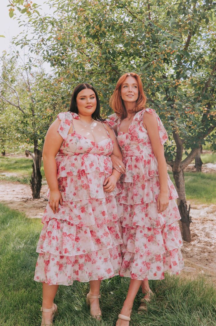 two women standing next to each other in front of an apple tree wearing matching dresses