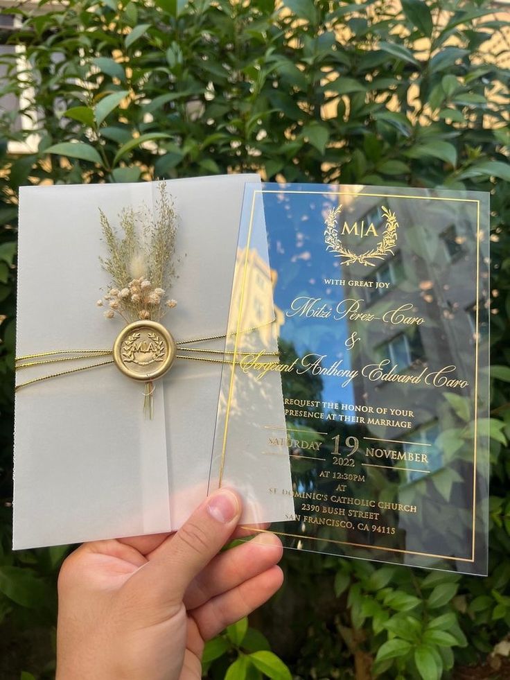 a person holding up a wedding card in front of some bushes and trees with the word mia on it