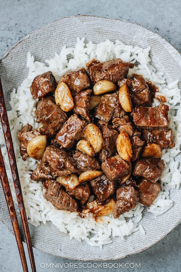 a white plate topped with meat and rice next to chopsticks