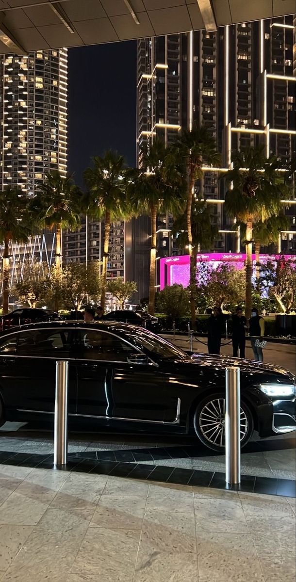 a black car parked on the side of a road next to tall buildings at night