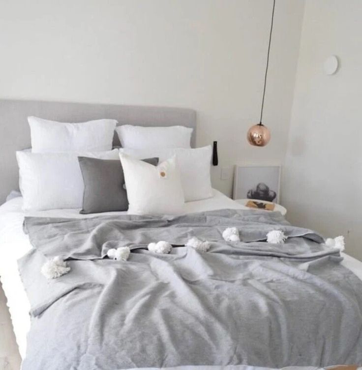 a bed with pillows and blankets on it in a white room, next to a lamp