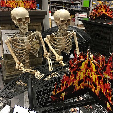 two skeletons sitting on top of a shopping cart next to a flamed object in a store