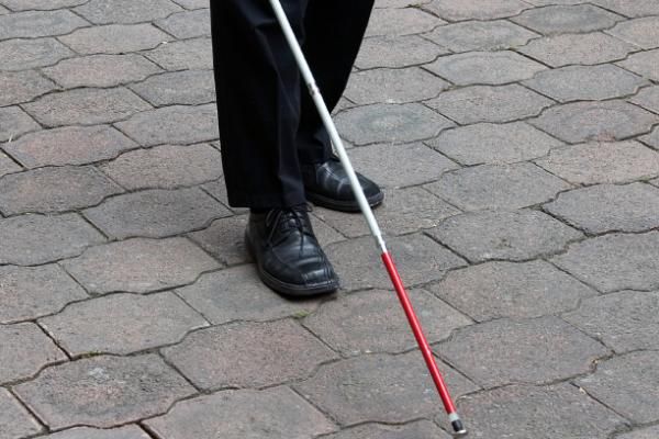 a man is standing on the sidewalk with a cane in his hand and wearing black shoes