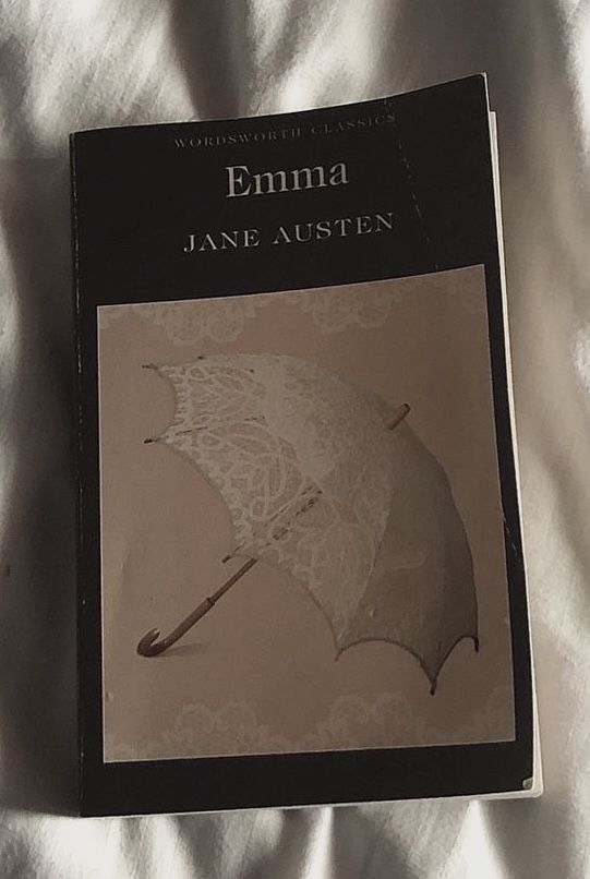 a book with an umbrella on it laying on top of a white bed coverlet