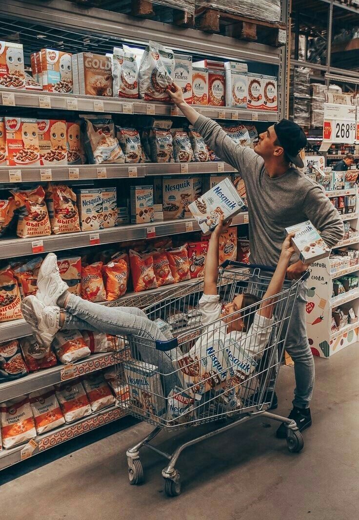 a man and woman in a grocery store pushing a shopping cart with their legs up