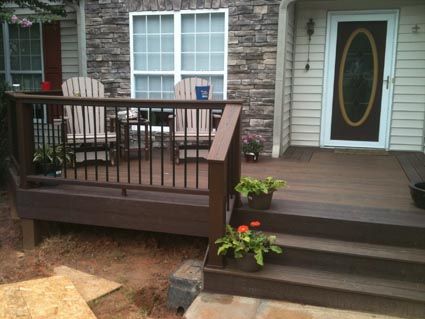 a wooden deck in front of a house with chairs and flowers on the steps next to it