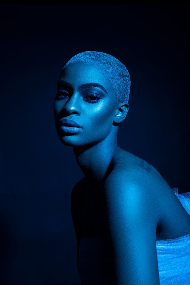 a woman with blue makeup is posing for a photo in front of a dark background