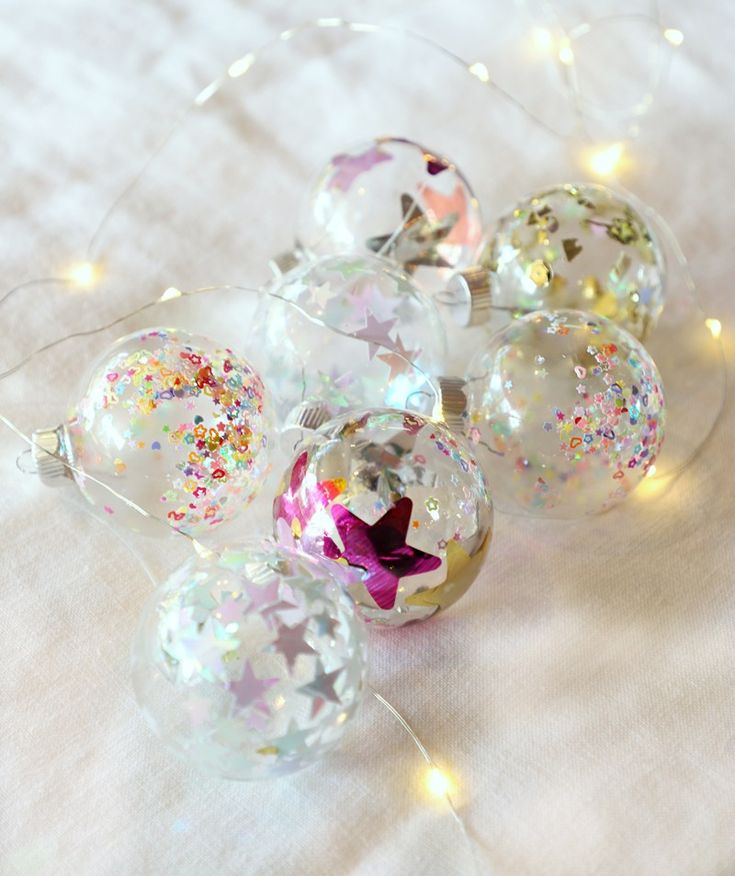 some glass balls with glitter on them sitting on a white table cloth and lights are shining in the background