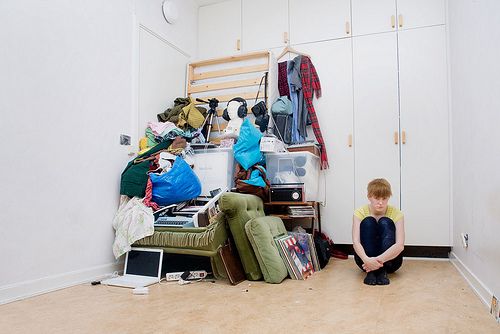 a young boy sitting on the floor in front of a room full of clutter