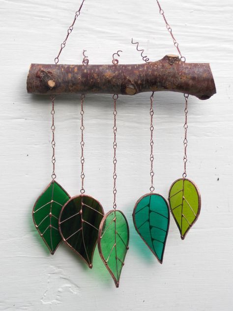 three green leaves hanging from a branch on a white wall next to a piece of wood