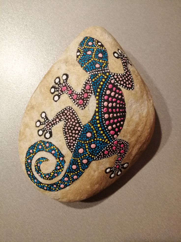 a painted rock sitting on top of a counter next to a white table with a black and blue lizard on it