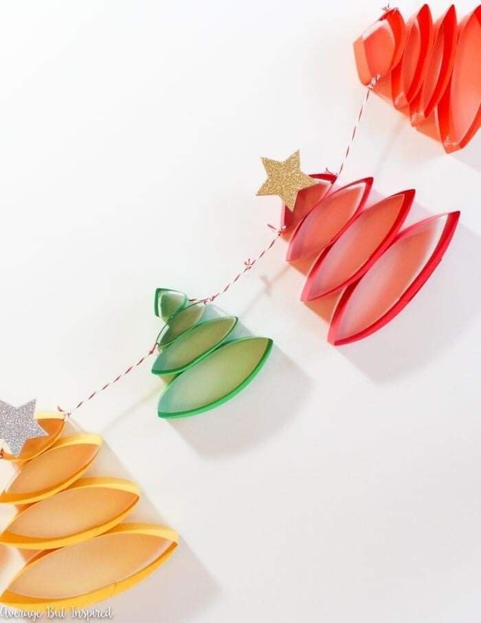 paper christmas tree decorations hanging from string on white wall with star decoration above them,