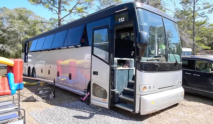 a bus that is parked next to some other cars in the dirt and trees behind it