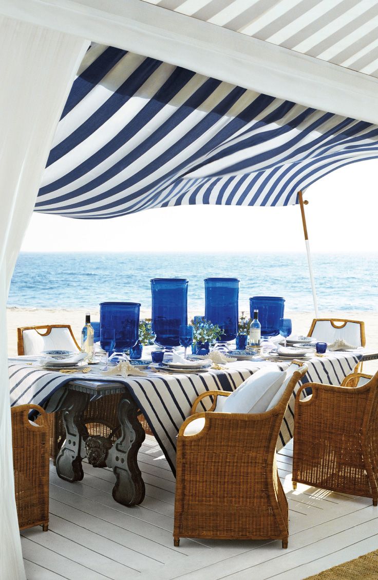 an outdoor dining area on the beach with blue and white striped umbrellas over it