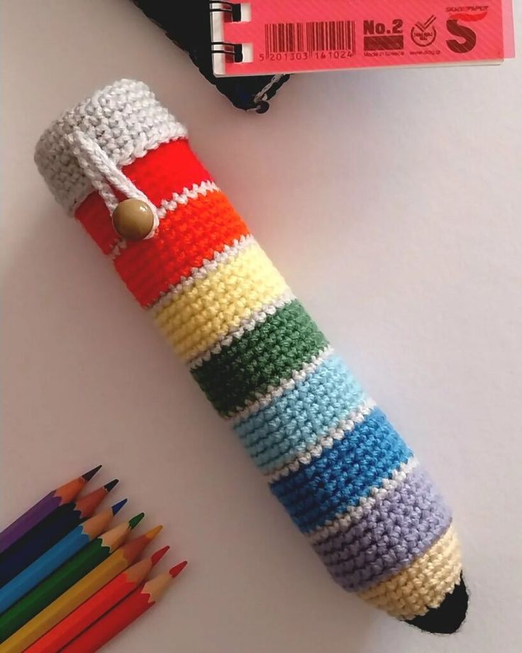 a crocheted pencil holder with colored pencils next to it and a book