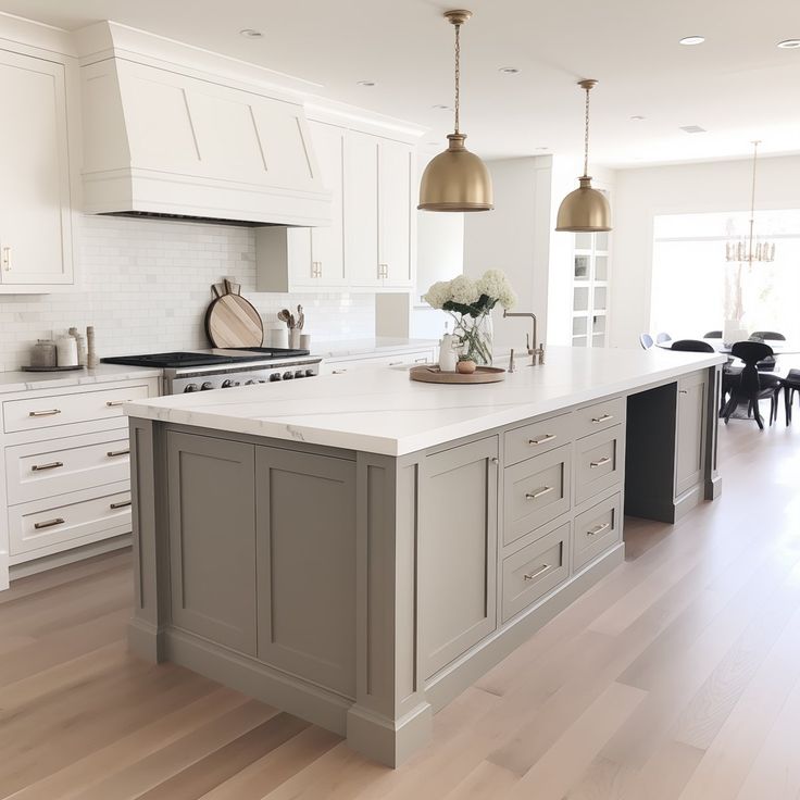 a large kitchen with white cabinets and wood flooring is pictured in this image, there are two pendant lights hanging over the island