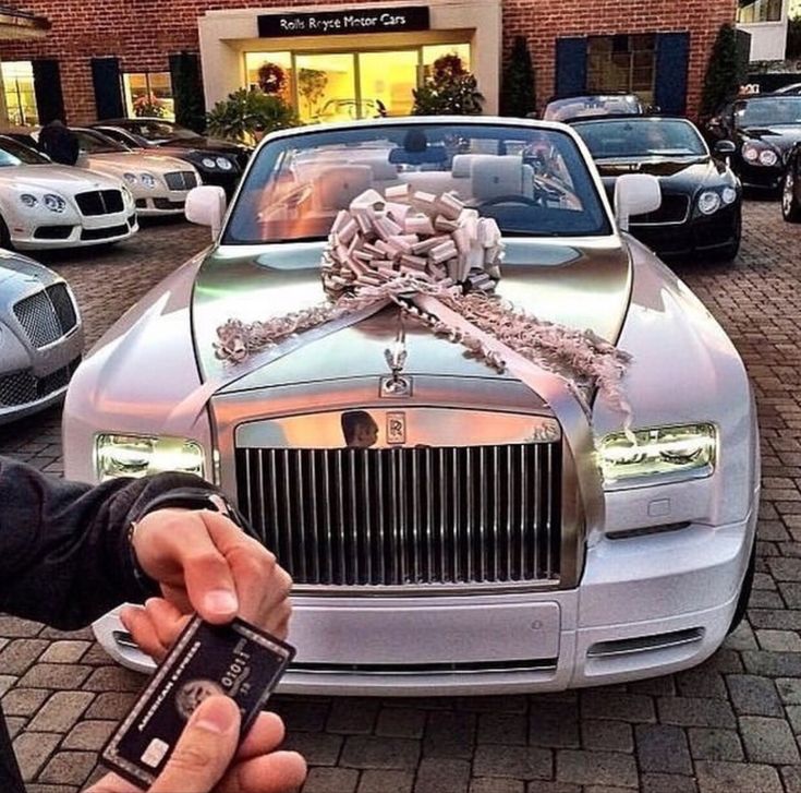 a person holding a cell phone in front of a rolls royce parked on the street