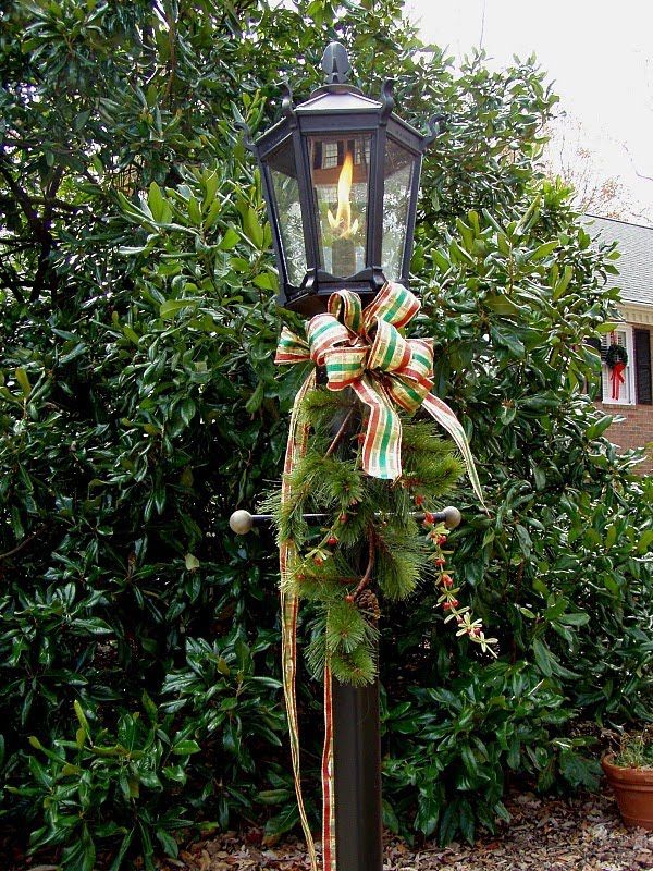 a lamp post with a bow on it in front of some bushes and trees,