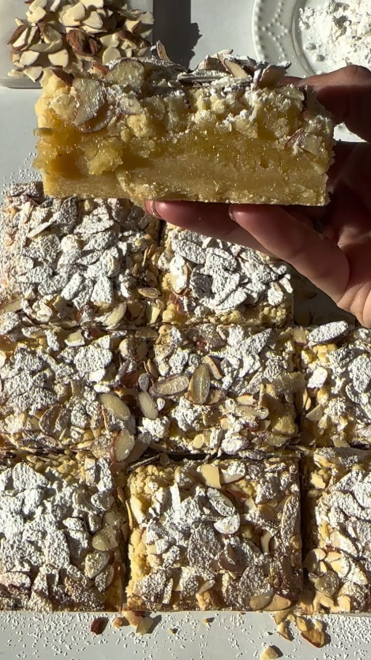 a person is holding up a piece of cake with powdered sugar and nuts on top