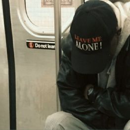 a man wearing a hat sitting on a subway car next to another person with his head in his hands